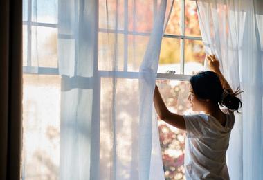 Canadian homeowner opening her living room windows to let in fresh air and natural sunlight, representing healthy home ventilation