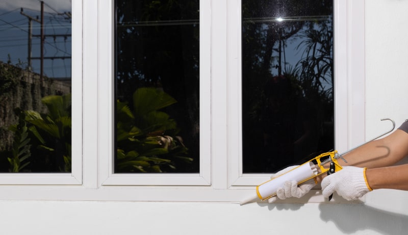 Handyman applying exterior sealant to a casement window for weatherproofing