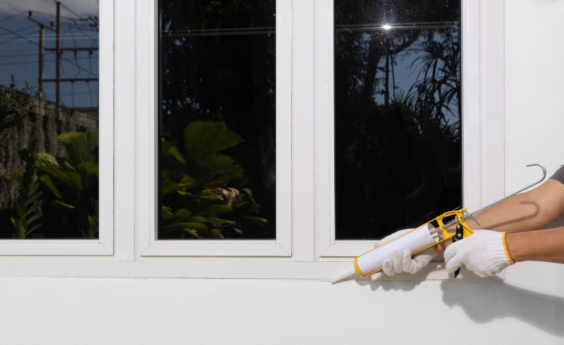 Technician sealing exterior casement window frame on house