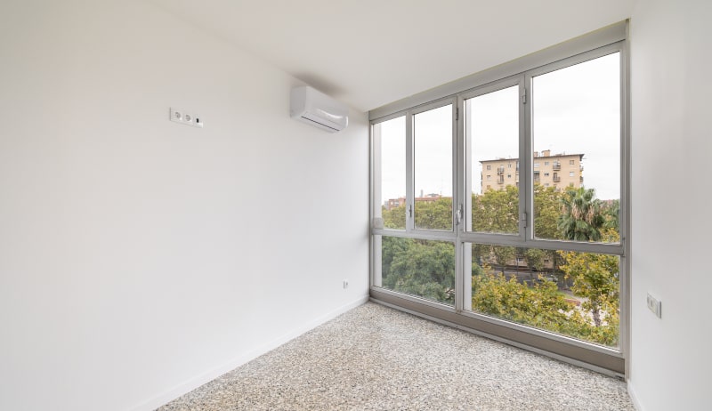Spacious empty room with white walls and tall floor-to-ceiling windows letting in daylight